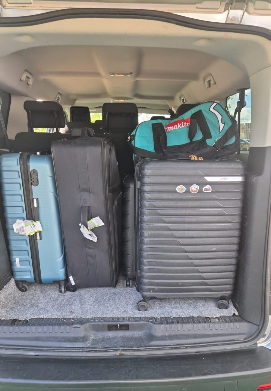Hard-shell suitcases and a holdall standing in the open boot of a minibus.